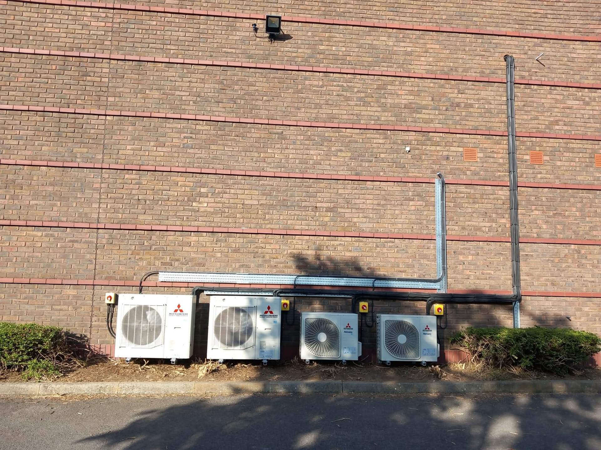Four Mitsubishi Electric commercial air conditioning condensers installed outside industrial building