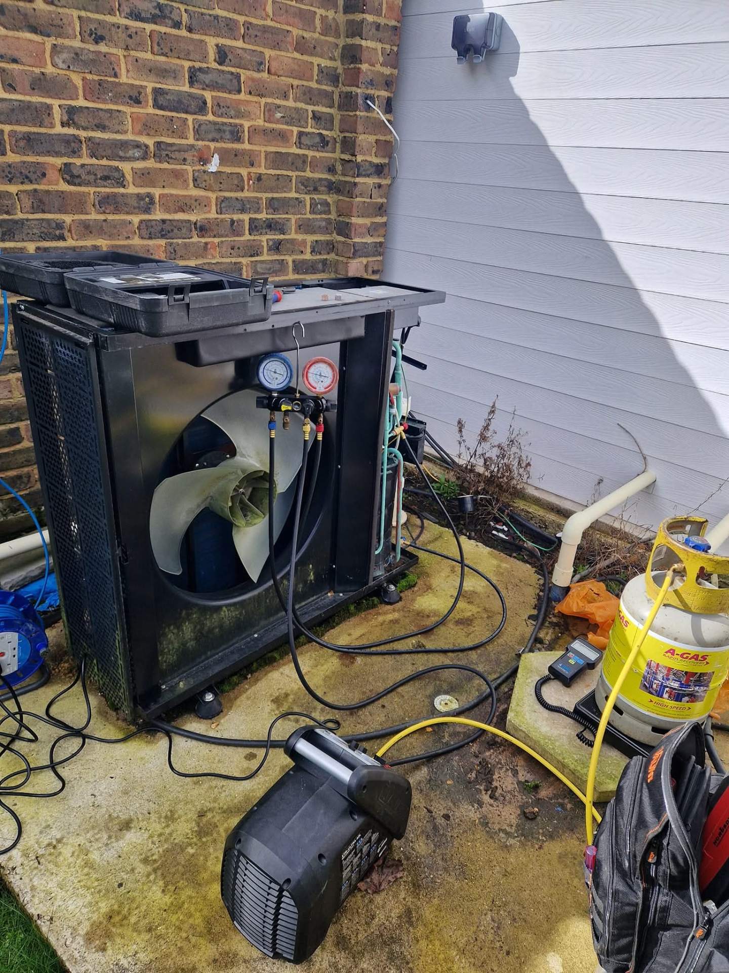 Swimming pool heat pump repair in progress with refrigerant manifold gauges, vacuum pump, and recovery equipment