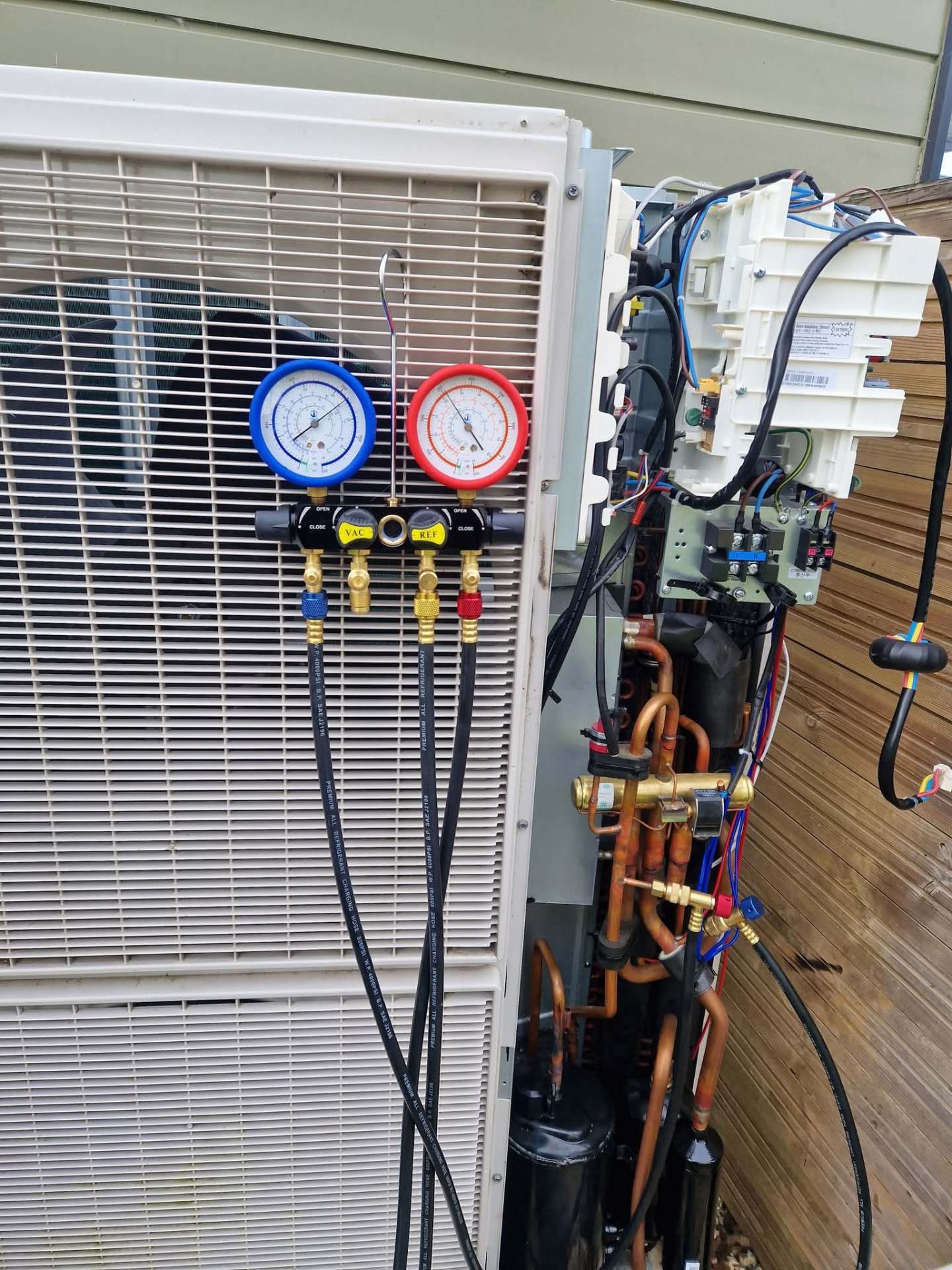 Heat pump diagnostic — refrigerant manifold gauges and open compressor compartment showing internal copper pipework and electrical connections