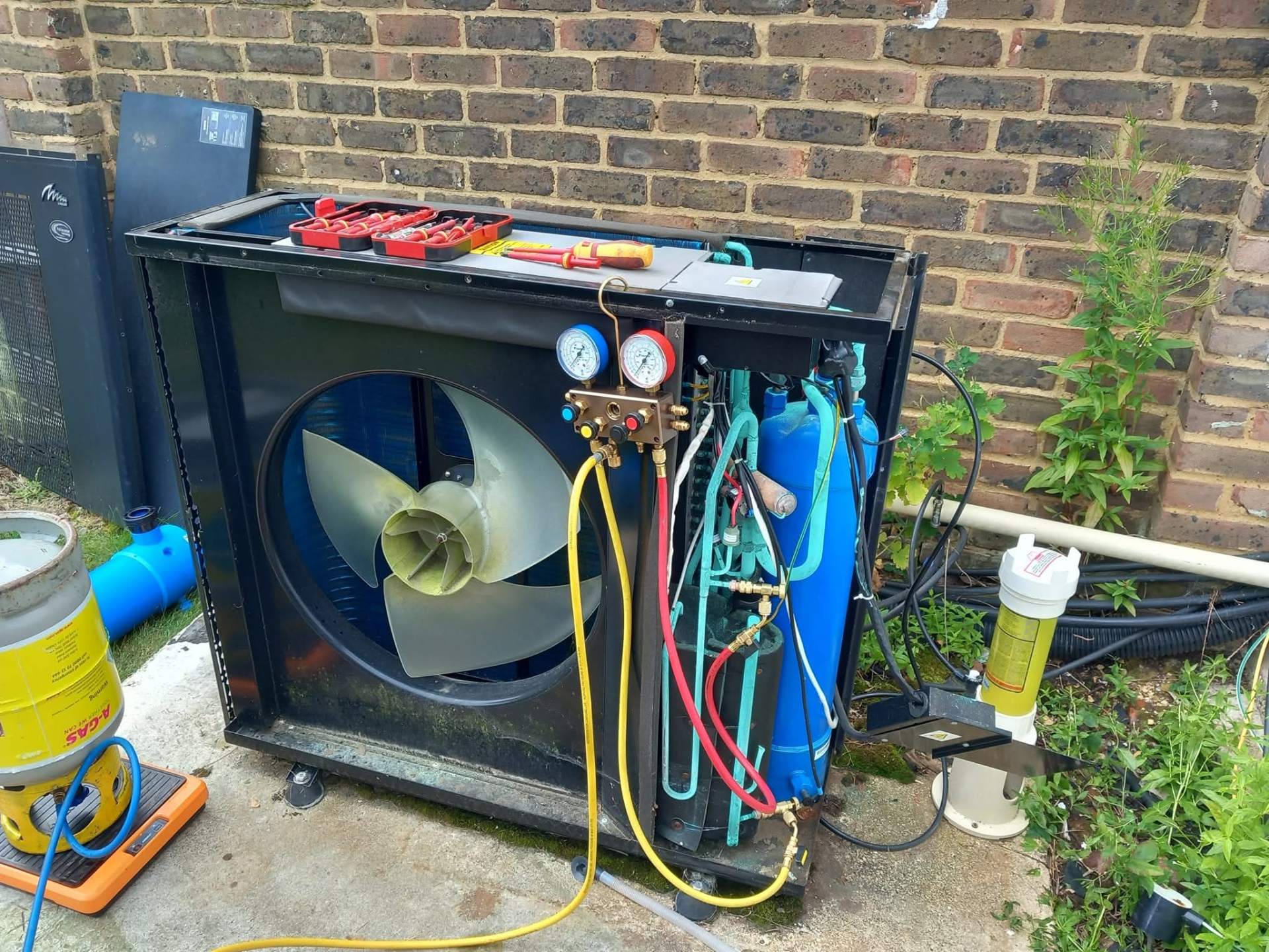 Swimming pool heat pump stripped down for repair with refrigerant gauges, nitrogen cylinder, and brazing equipment